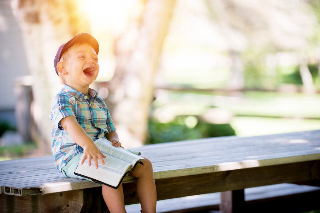Boy holding book and laughing while sitting on a bench